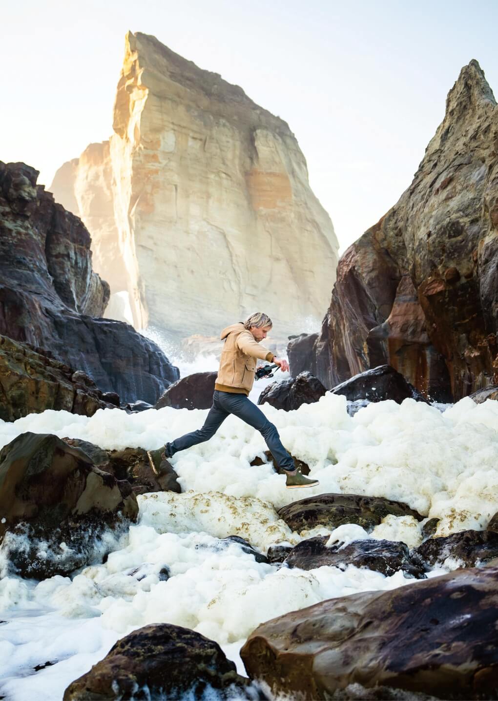 Ben Moon jumps between rocks and over foam on the shore